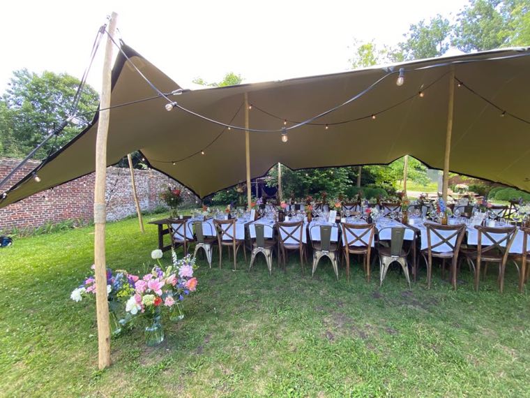 Gezelschap aan lange tafels onder een tent in de tuin